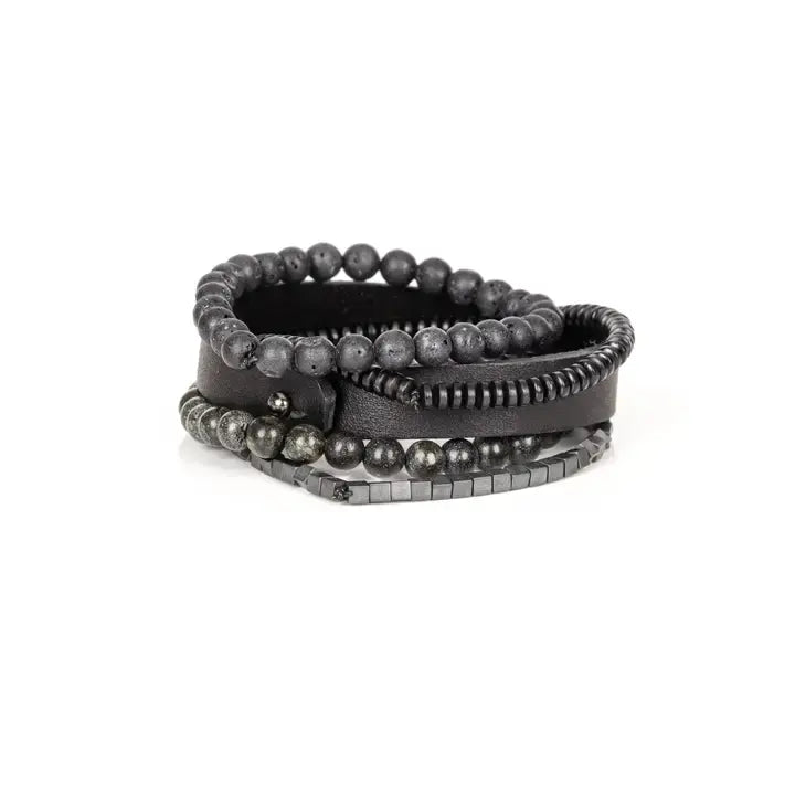 Men’s layered bracelet set featuring a black leather cuff, matte black lava stone beads, dark gray natural stone beads, black heishi spacers, faceted black crystal beads, and hematite cube beads, stacked in a sophisticated monochromatic luxury design on a white background.