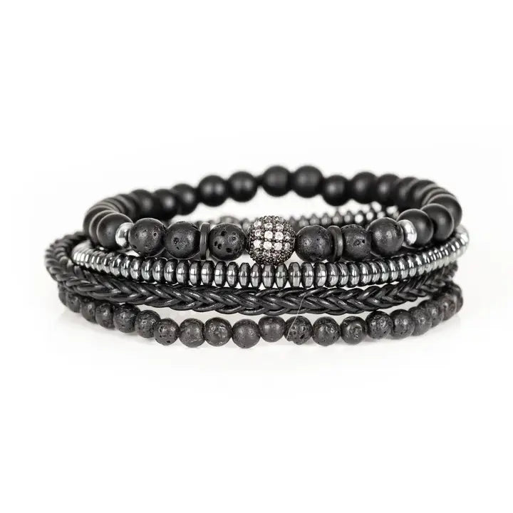 Black layered men’s bracelet set with lava stone beads, braided leather, hematite accents, matte black beads, and pavé centerpiece on white background.