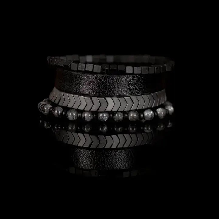 Men’s layered bracelet set featuring a black textured leather cuff, gunmetal cube bead bracelet, gunmetal chevron metal beads, and gray marbled natural stone beads, stacked in a bold industrial luxury design on a white background.