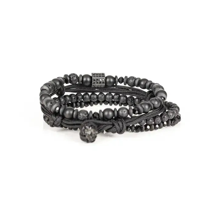 Black layered men’s bracelet set with lava stone beads, matte black beads, crystal accents, braided rope wraps, and pavé square centerpiece on white background.