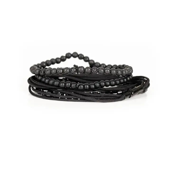 Black layered men’s bracelet set with lava stone beads, geometric crystal cube accents, matte black beads, polished centerpiece, and braided rope wraps on white background.