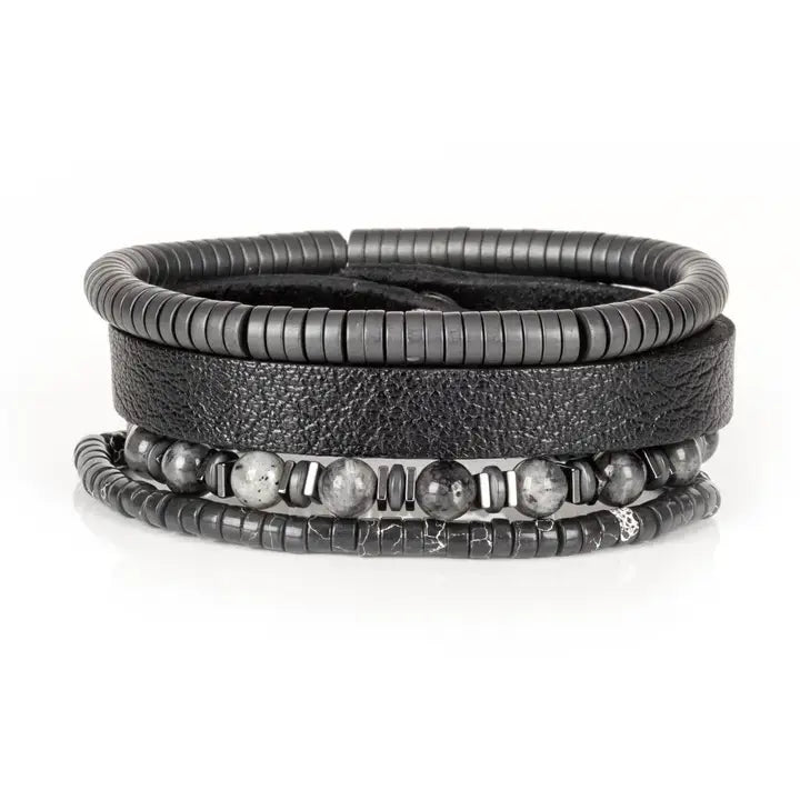 Black multi-layer men’s bracelet featuring textured leather band, gunmetal hematite bead strands, matte grey stone beads, and layered metallic accents on a light background.