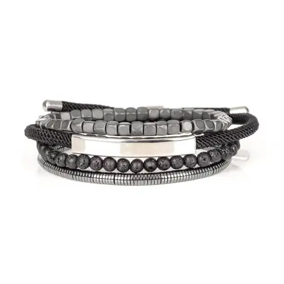 Men’s layered bracelet set featuring a polished silver-tone ID bar centerpiece, matte black lava stone beads, gunmetal cube beads, black braided cord wraps, and silver-tone coil wrap accents, stacked in a sleek industrial luxury design on a white background.