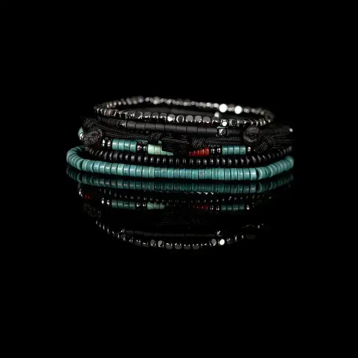 Black multi-layer men’s bracelet featuring hematite bead strands, braided rope layers, turquoise and red accent beads, geometric black centerpiece, and layered metallic details on a light background.