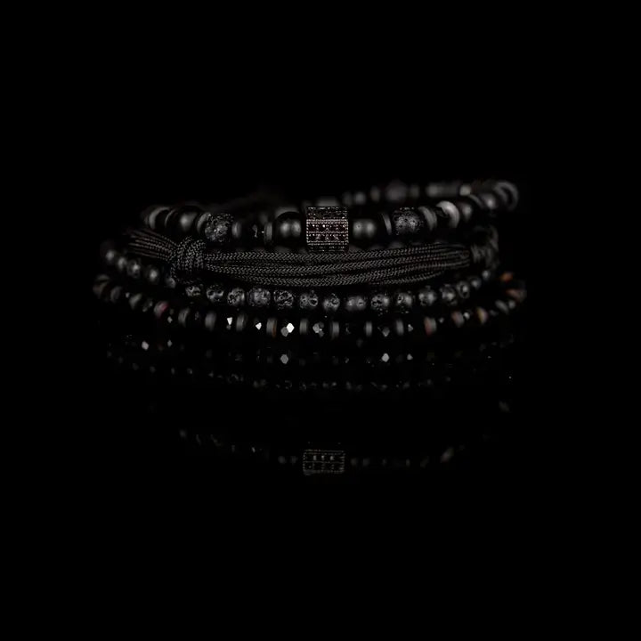 Black layered men’s bracelet set with lava stone beads, matte black beads, crystal accents, braided rope wraps, and pavé square centerpiece on white background.