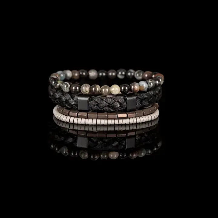 Black multi-layer men’s bracelet set featuring braided leather band, smoky grey natural stone beads, hematite cube accents, and layered metallic bead strands on a light background.