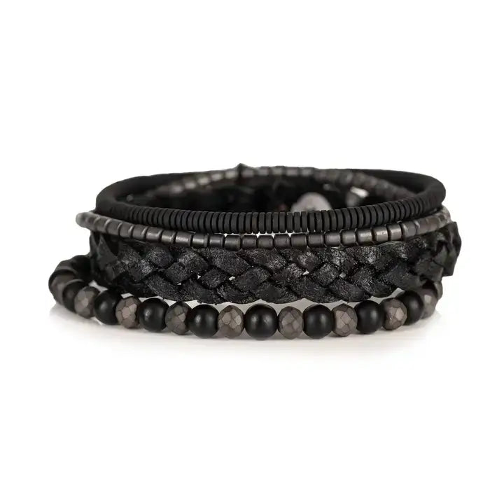 Black multi-layer men’s bracelet featuring braided leather, matte black onyx beads, faceted hematite stones, and layered metallic accents on a light background.