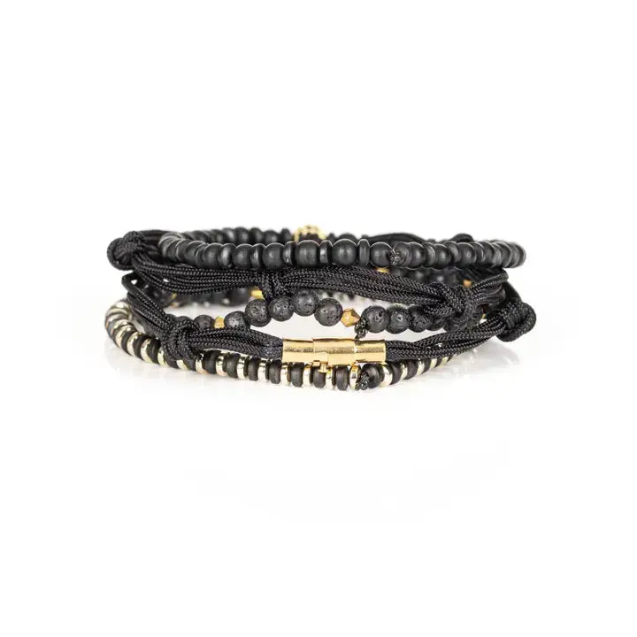 Black and gold layered men’s bracelet set with matte black beads, lava stone accents, gold pavé centerpiece bead, metallic spacers, and braided rope wraps on white background.