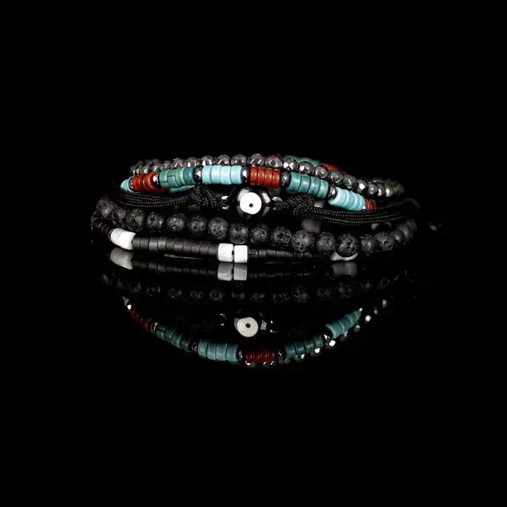Men’s layered bracelet set featuring matte black lava stone beads, faceted hematite crystal beads, turquoise heishi beads, coral-red accent beads, black braided cord wraps, white and black spacer beads, and an evil eye centerpiece, stacked in a bold bohemian luxury design on a white background.