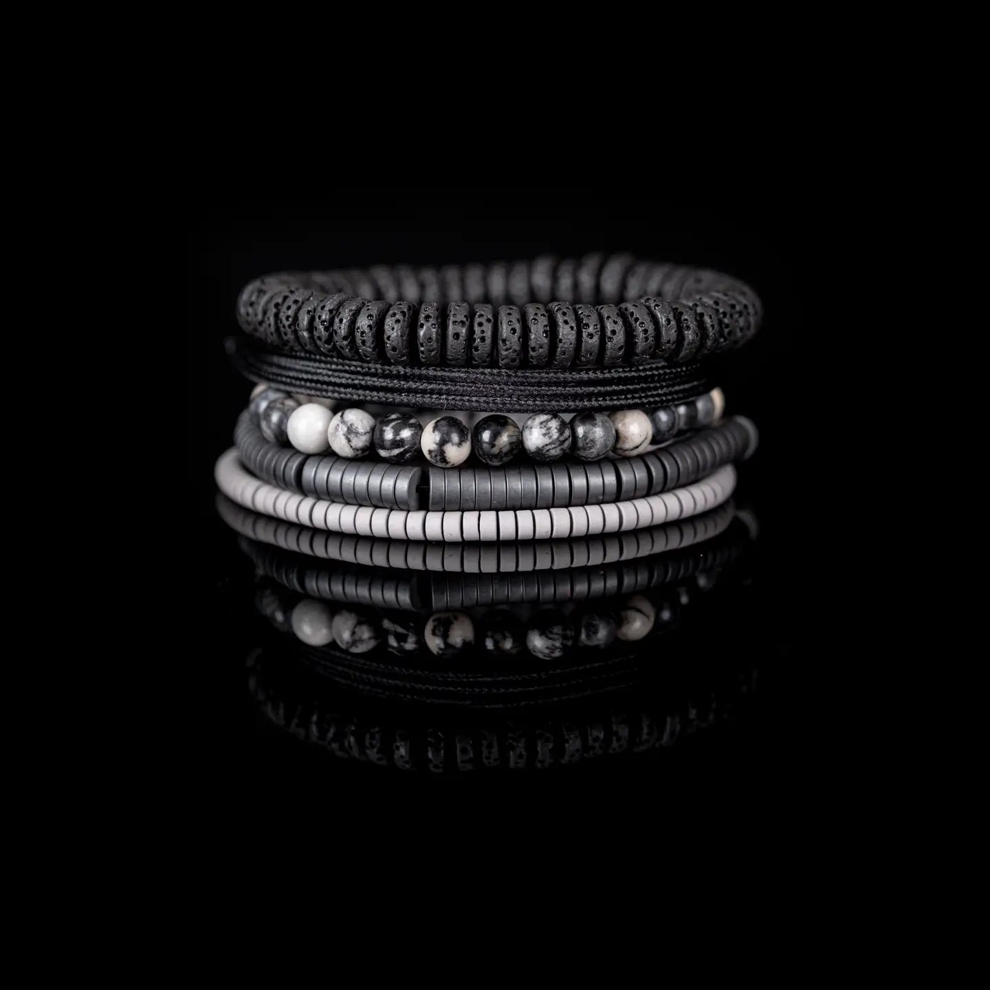 Men’s layered bracelet set featuring black lava stone disc beads, black braided cord wraps, white and gray marbled natural stone beads, black hematite coil beads, and light gray heishi beads, stacked in a sophisticated monochromatic luxury design on a white background.