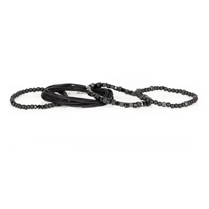 Black layered men’s bracelet set with matte black beads, faceted geometric crystal accents, cube beads, and braided rope wraps on white background