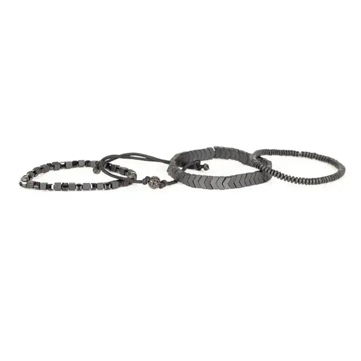 Men’s layered bracelet set featuring gunmetal chevron metal beads, black hematite cube beads, dark metallic heishi beads, black braided cord, and a pavé-style gunmetal accent bead, stacked in a sleek monochromatic luxury design on a white background.