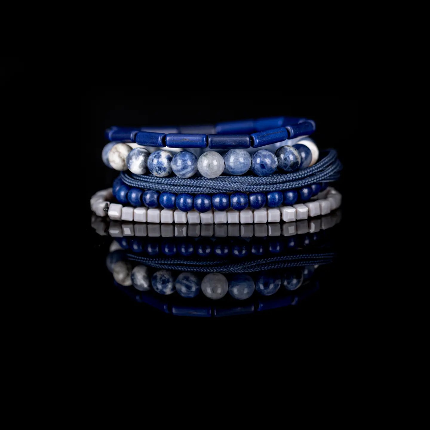 Men’s layered bracelet set featuring deep blue lapis-style beads, blue and white marbled natural stone beads, navy braided cord wraps, matte blue round beads, and light gray geometric heishi beads, stacked in a sophisticated nautical-inspired luxury design on a white background.