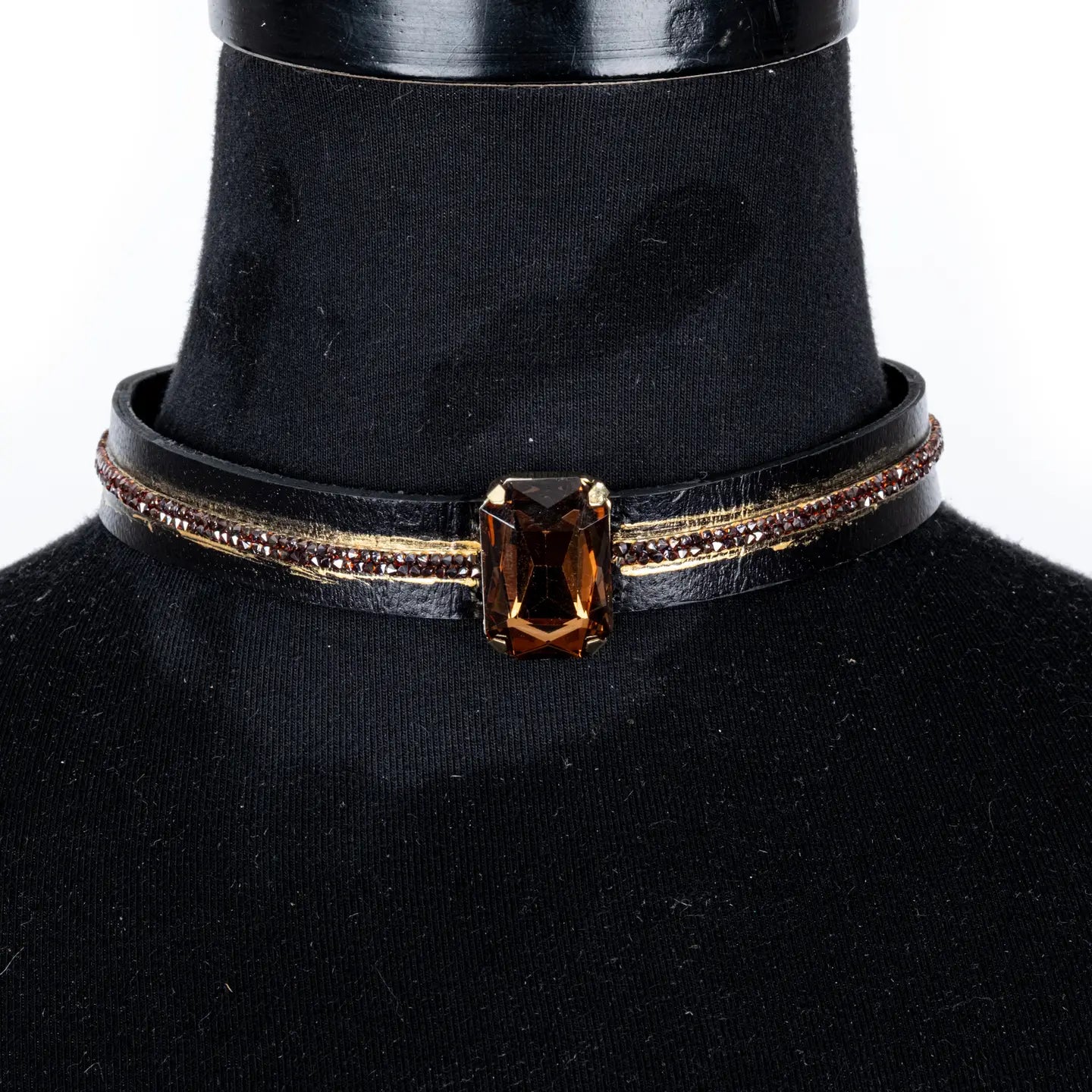 Black leather choker with a central brown rectangular crystal and fine rhinestone and gold detailing along the band, displayed on a white background.