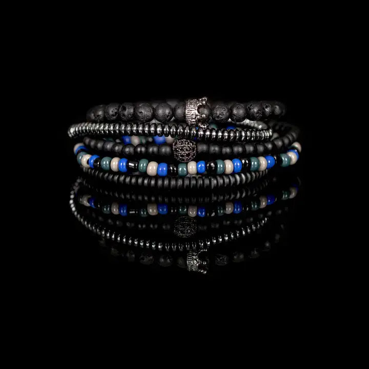 Black multi-layer men’s bracelet featuring lava stone beads, metallic hematite strands, crystal crown centerpiece, blue and white accent beads, and layered black bead details on a light background.