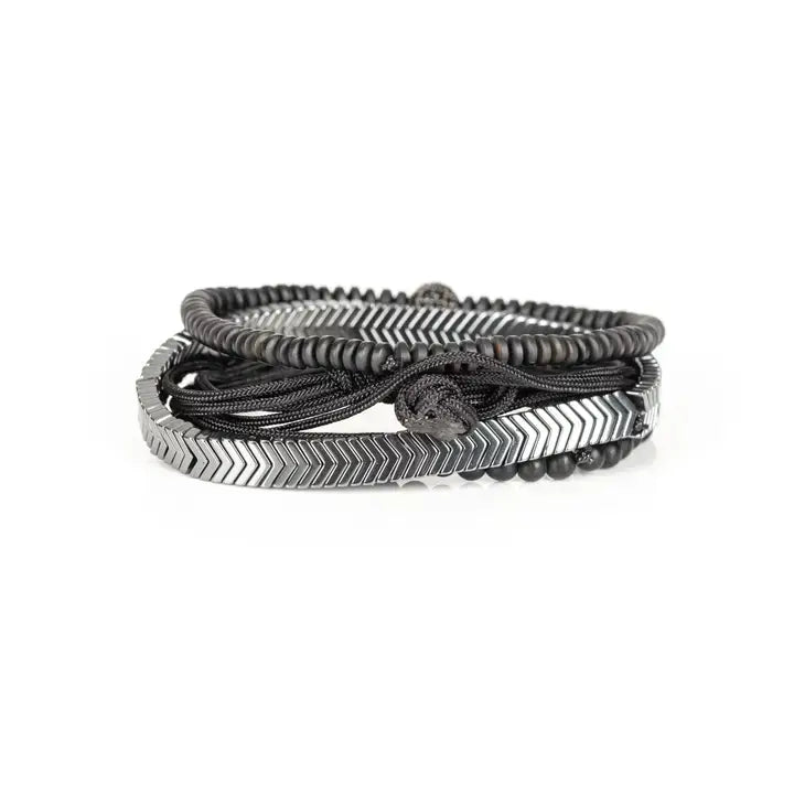 Black multi-layer men’s bracelet featuring silver chevron metal bar, hematite bead strands, crystal accent bead, faceted black stones, and braided black rope layers on a light background.