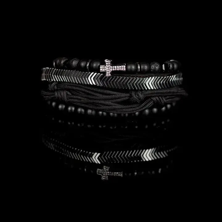 Black and silver layered men’s bracelet set with matte black beads, silver chevron metal bar, pavé cross detail, and braided rope wraps on white background.