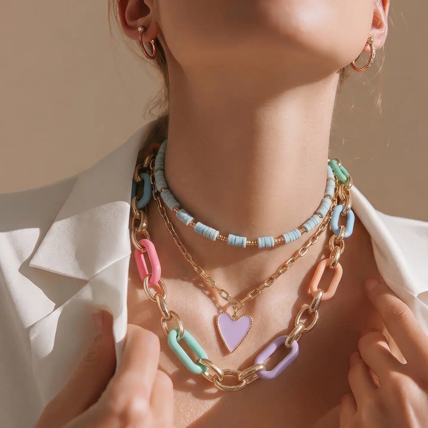 Layered pastel enamel chain necklace with gold links and a small heart pendant on a white background.