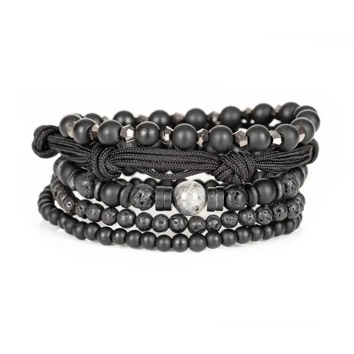 Black layered men’s bracelet set with matte black beads, lava stone accents, marbled centerpiece stone, faceted metallic beads, and braided rope wraps on white background.