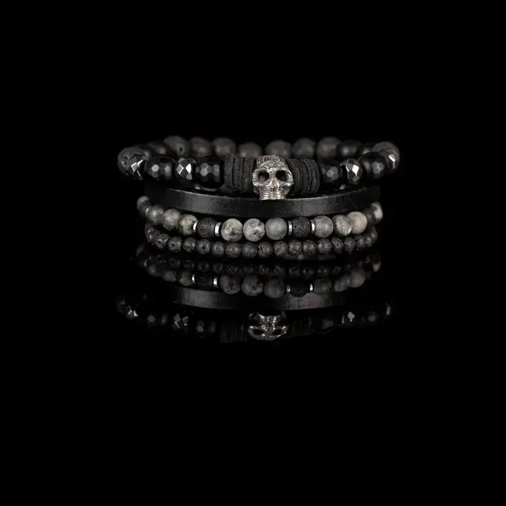 Black multi-layer men’s bracelet set featuring faceted black onyx beads, lava stone accents, black leather band, and silver skull centerpiece on a light background.
