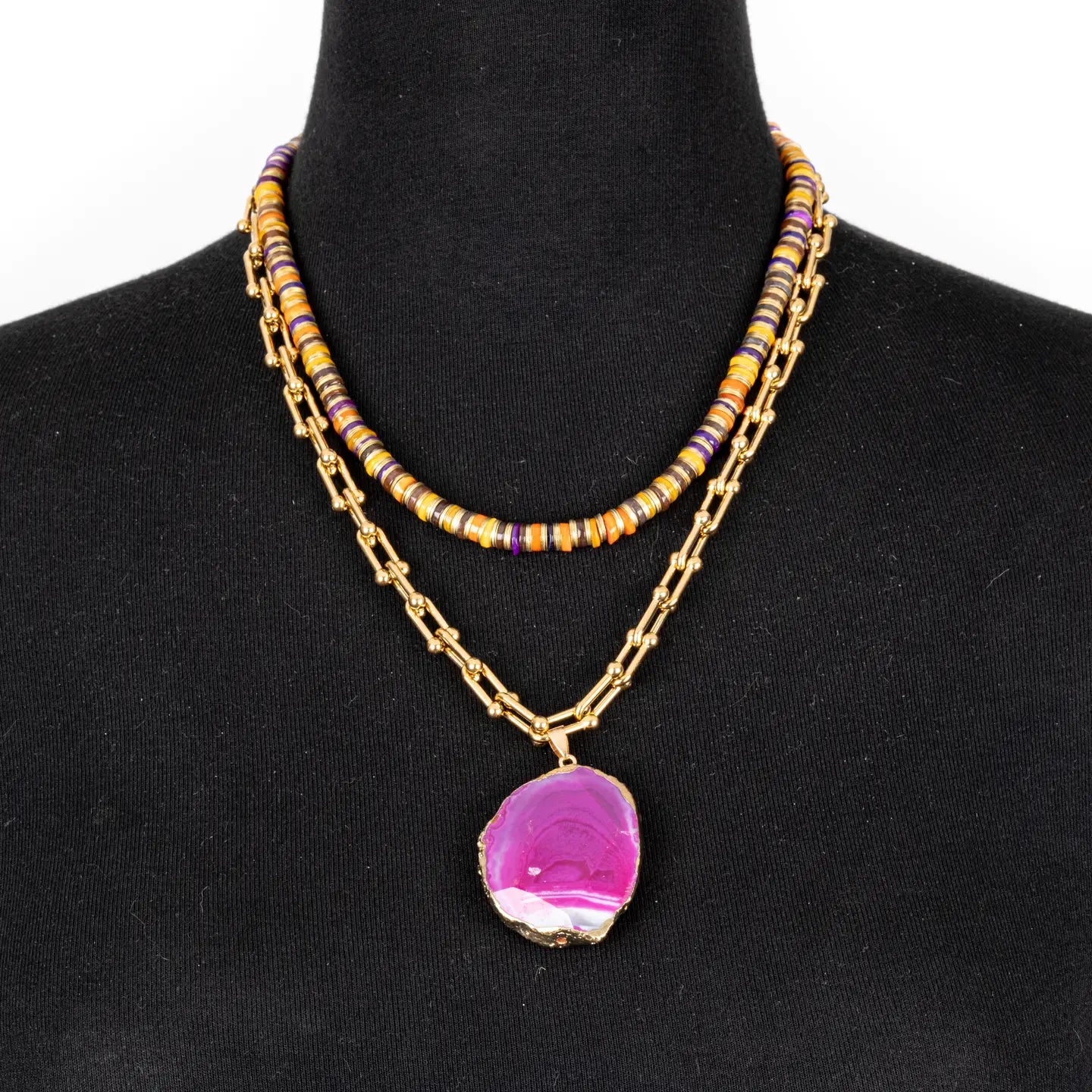 Layered necklace with multicolor beads and pink agate pendant on gold chain on white background.
