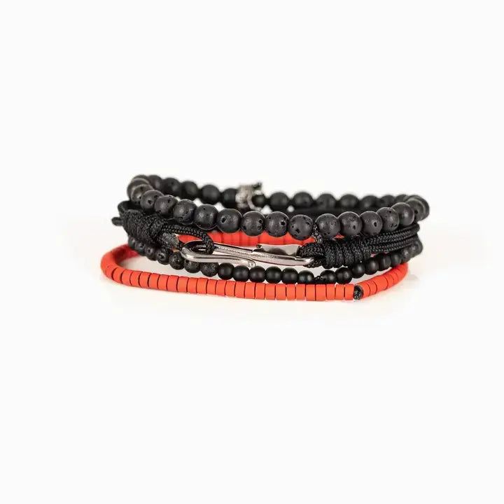 Men’s layered bracelet set featuring matte black lava stone beads, black braided cord, black onyx-style beads, gunmetal accent beads, a crown charm centerpiece, and vibrant red heishi beads, stacked in a bold contemporary luxury design on a white background.