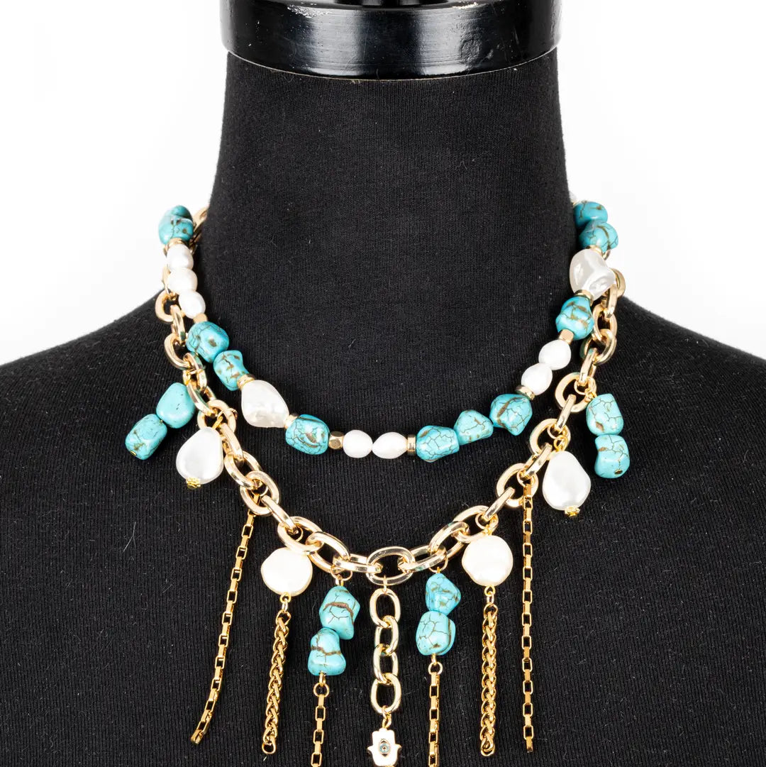 Layered turquoise and white beaded necklace with gold chain details and dangling chain accents on a white background.