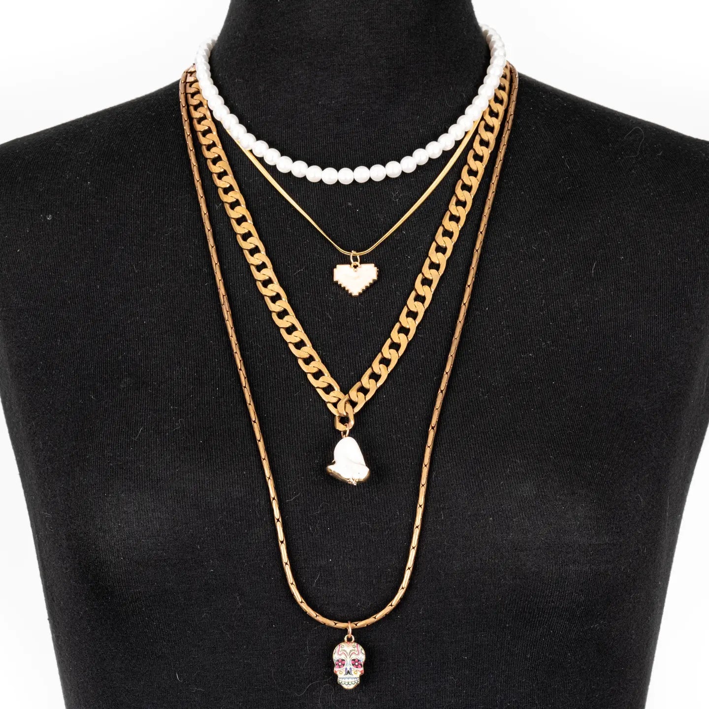 Layered gold necklace with white bead strand, heart charms, and skull pendant on white background.