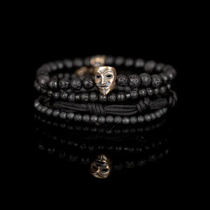 Black layered men’s bracelet set with lava stone beads, matte black beads, metallic mask centerpiece, faceted crystal accents, and braided rope wraps on white background.