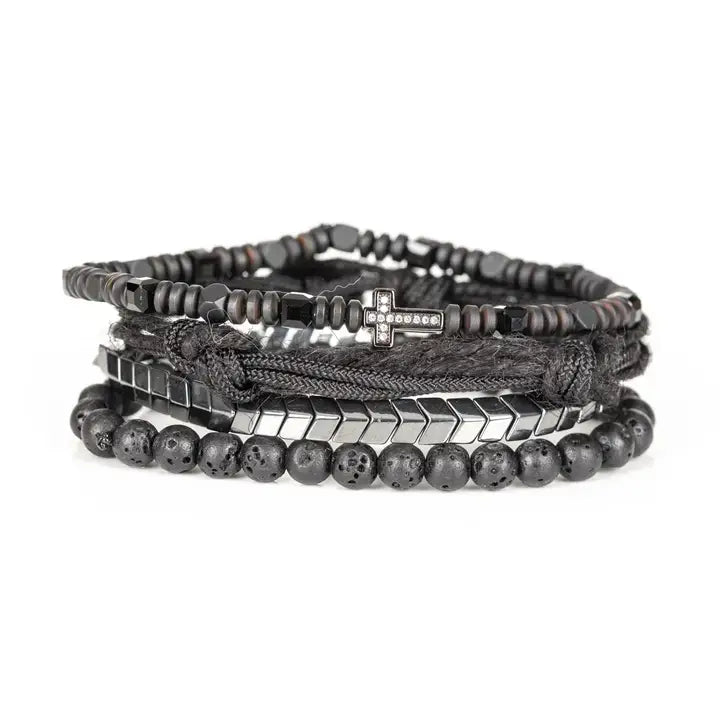 Black layered men’s bracelet set with lava stone beads, pavé cross detail, silver chevron metal strand, braided rope wraps, and woven texture accents on white background.