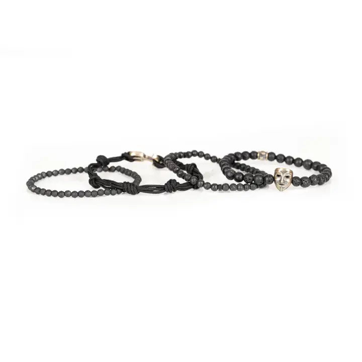 Black layered men’s bracelet set with lava stone beads, matte black beads, metallic mask centerpiece, faceted crystal accents, and braided rope wraps on white background.
