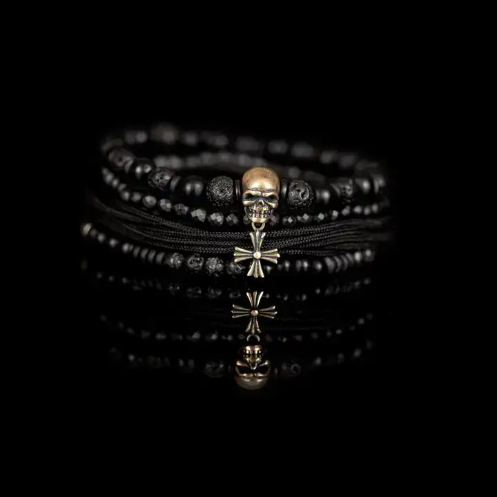 Black multi-layer men’s bracelet set featuring lava stone beads, matte onyx, faceted black stones, braided rope layers, metallic skull centerpiece, and cross accent on a light background.