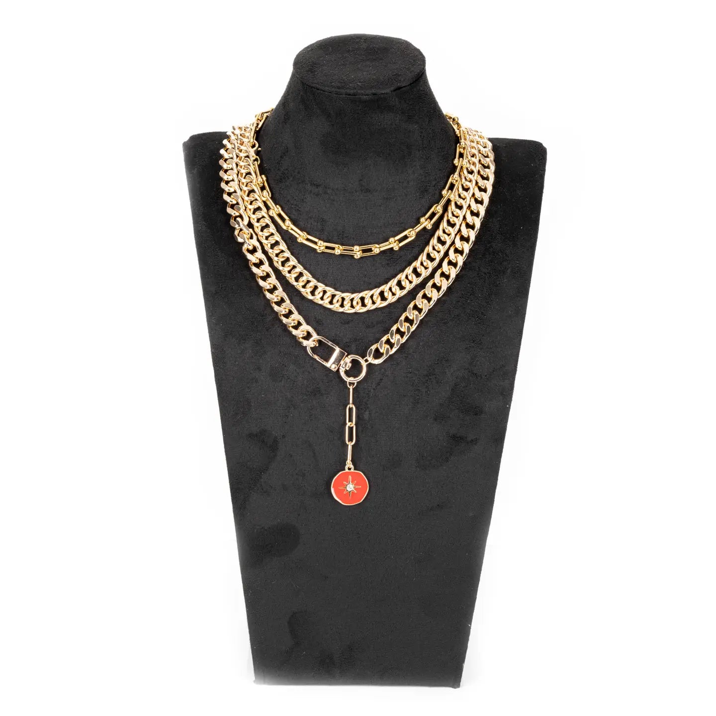 Layered gold chain necklace with multiple chain styles and a red enamel charm drop, displayed on a white background.