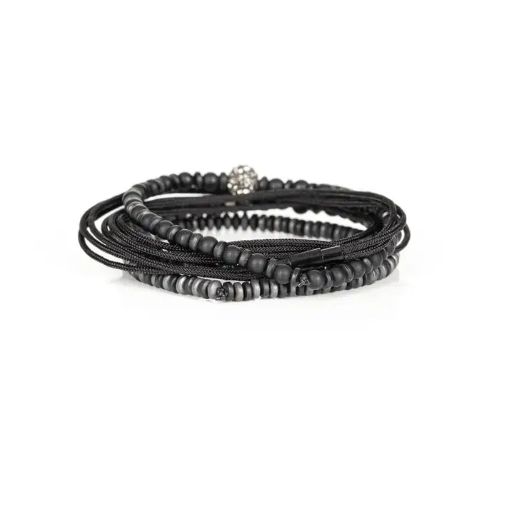 Black multi-layer men’s bracelet featuring matte black beads, lava stone accents, crystal centerpiece bead, braided rope layers, faceted metallic details, and hematite disc strands on a light background.