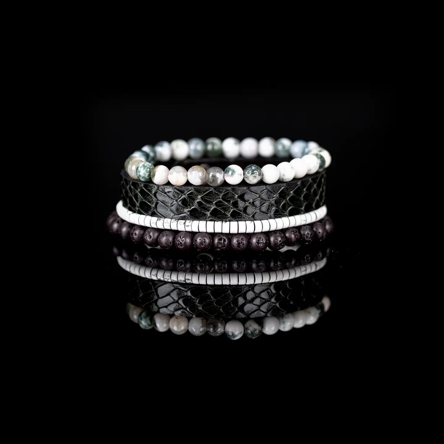 Men’s layered bracelet set featuring a black embossed leather cuff with a reptile-inspired texture, white howlite beads, green moss agate stone beads, white heishi beads, and dark lava stone beads, stacked in a sophisticated natural luxury design on a white background.