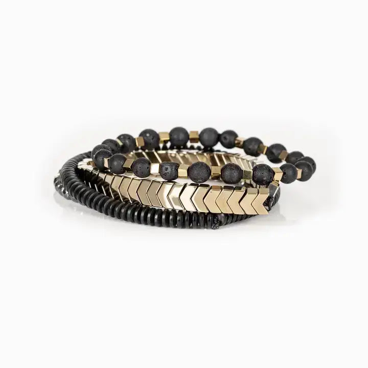 Men’s layered bracelet set featuring gold-tone chevron metal beads, matte black lava stone beads with gold-tone spacers, black heishi beads, and faceted hematite crystal beads, stacked in a sophisticated black and gold luxury design on a white background.
