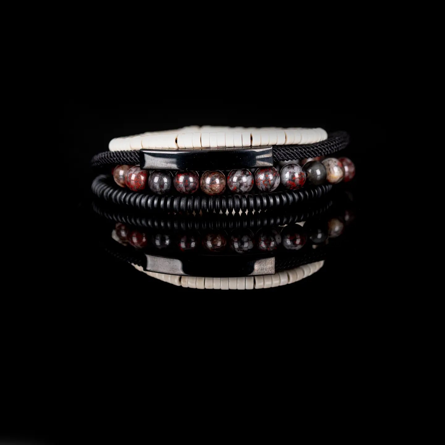 Men’s layered bracelet set featuring white howlite heishi beads, a gunmetal ID bar centerpiece, black braided cord wraps, red and black natural stone beads, and black coil wrap accents, stacked in a bold contemporary luxury design on a white background.