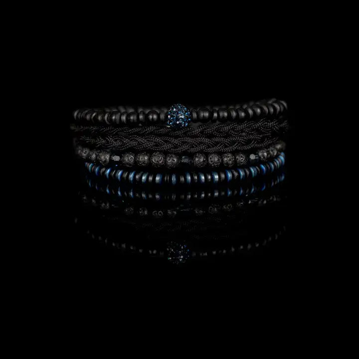 Black and blue multi-layer men’s bracelet featuring braided rope layers, lava stone beads, blue crystal centerpiece bead, faceted crystal accents, and blue metallic disc details on a light background.