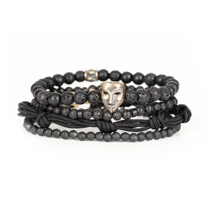 Black layered men’s bracelet set with lava stone beads, matte black beads, metallic mask centerpiece, faceted crystal accents, and braided rope wraps on white background.