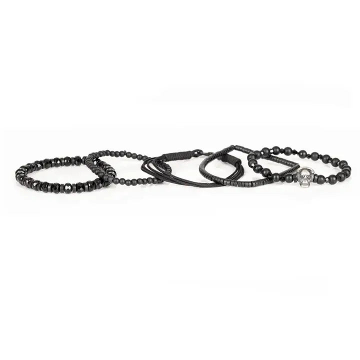 Black layered men’s bracelet set with matte black beads, silver skull centerpiece, faceted crystal accents, and braided rope wraps on white background.