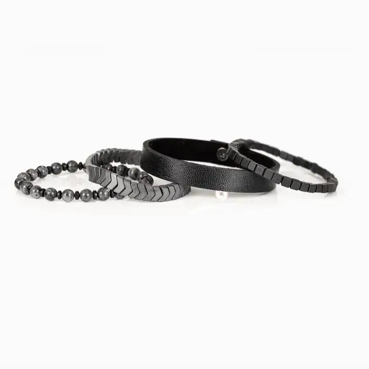 Men’s layered bracelet set featuring a black textured leather cuff, gunmetal cube bead bracelet, gunmetal chevron metal beads, and gray marbled natural stone beads, stacked in a bold industrial luxury design on a white background.