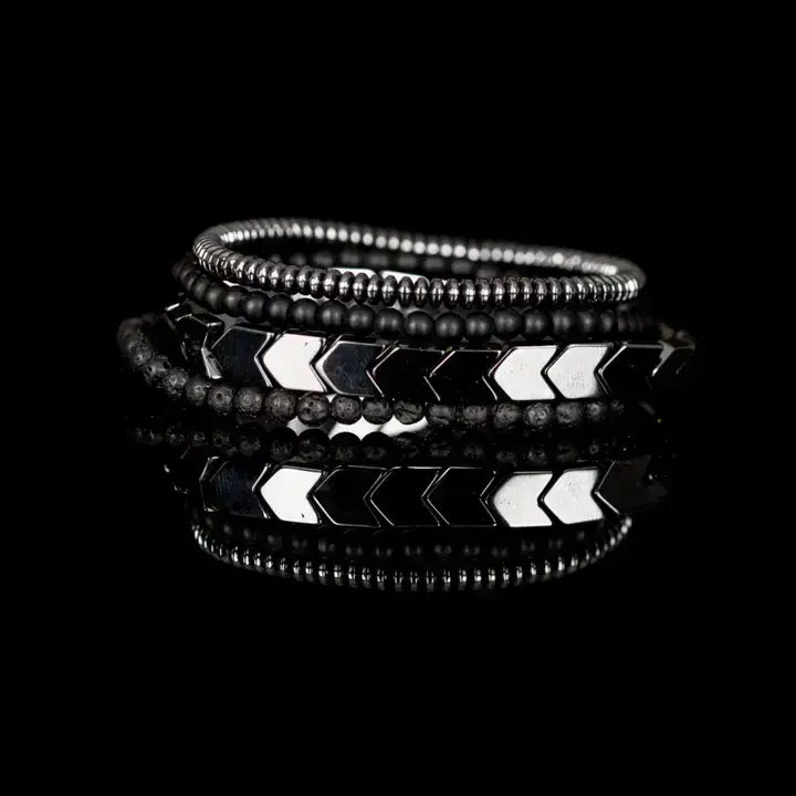 Men’s layered bracelet set featuring gunmetal chevron metal beads, matte black lava stone beads, black matte bead strands, and silver-tone hematite spacer beads, stacked in a bold industrial luxury design on a white background.