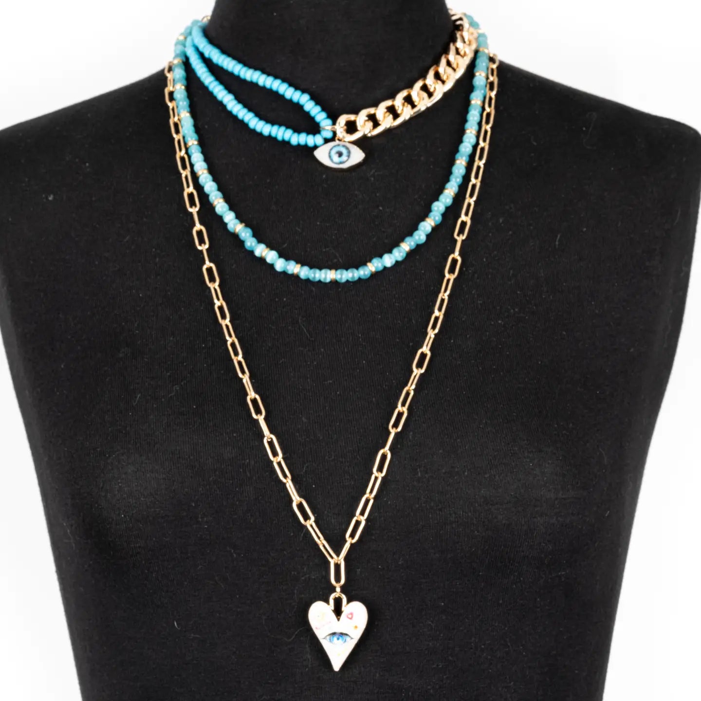 Layered turquoise and gold necklace with evil eye charm and heart pendant on white background.