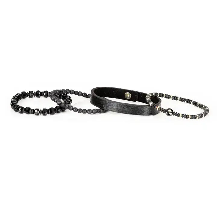 Men’s layered bracelet set featuring a black textured leather cuff, matte black lava stone beads, faceted black crystal beads, hematite accents, and a black beaded strand with a cross charm, stacked in a bold modern luxury design on a white background.