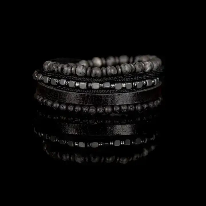 Men’s layered bracelet set featuring gray marbled natural stone beads, a black leather cuff, matte black lava stone beads, black braided cord, hematite cube beads, and metallic spacer accents, stacked in a sophisticated monochromatic luxury design on a white background.