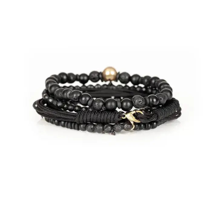 Black multi-layer men’s bracelet set featuring lava stone beads, matte onyx, faceted black stones, braided rope layers, metallic skull centerpiece, and cross accent on a light background.