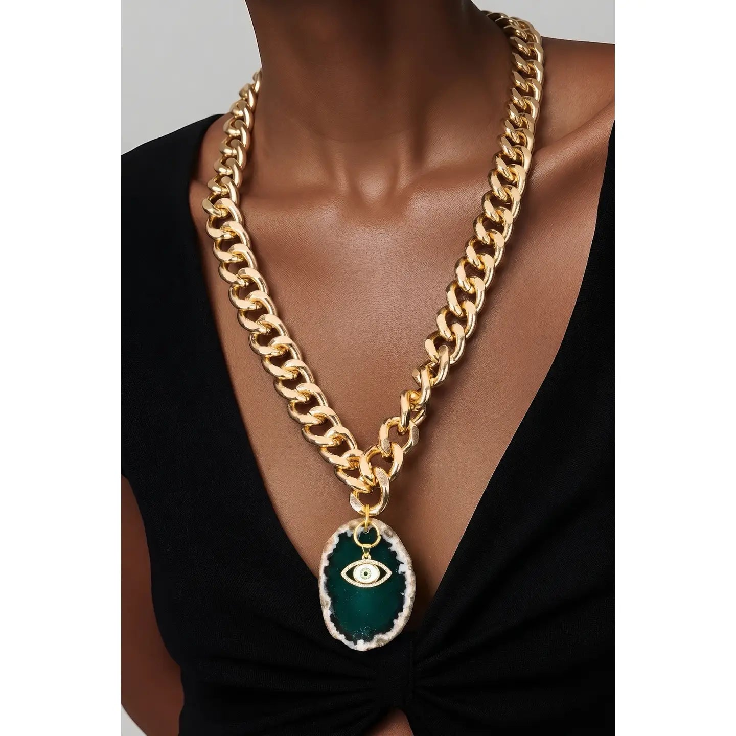 Gold chunky chain necklace with green stone pendant and evil eye charm on white background.