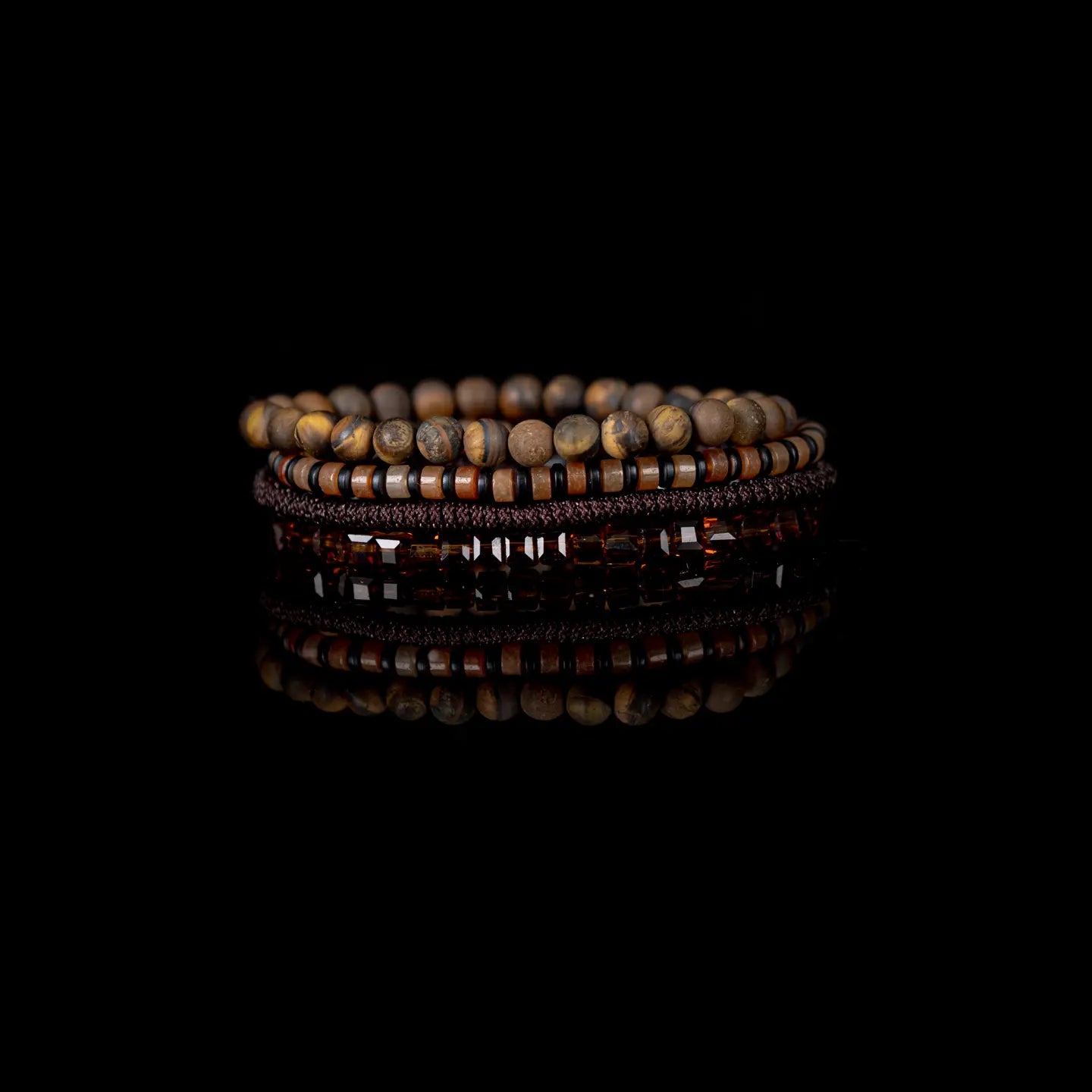 Men's layered bracelet set featuring genuine Tiger Eye stone beads, amber crystal accents, earth-tone heishi beads, and brown woven cord details arranged in a stacked design on a white background.
