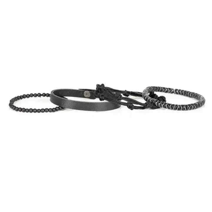 Black multi-layer men’s bracelet featuring hematite disc beads, braided black rope layers, smooth black leather band, and matte black bead strand on a light background.