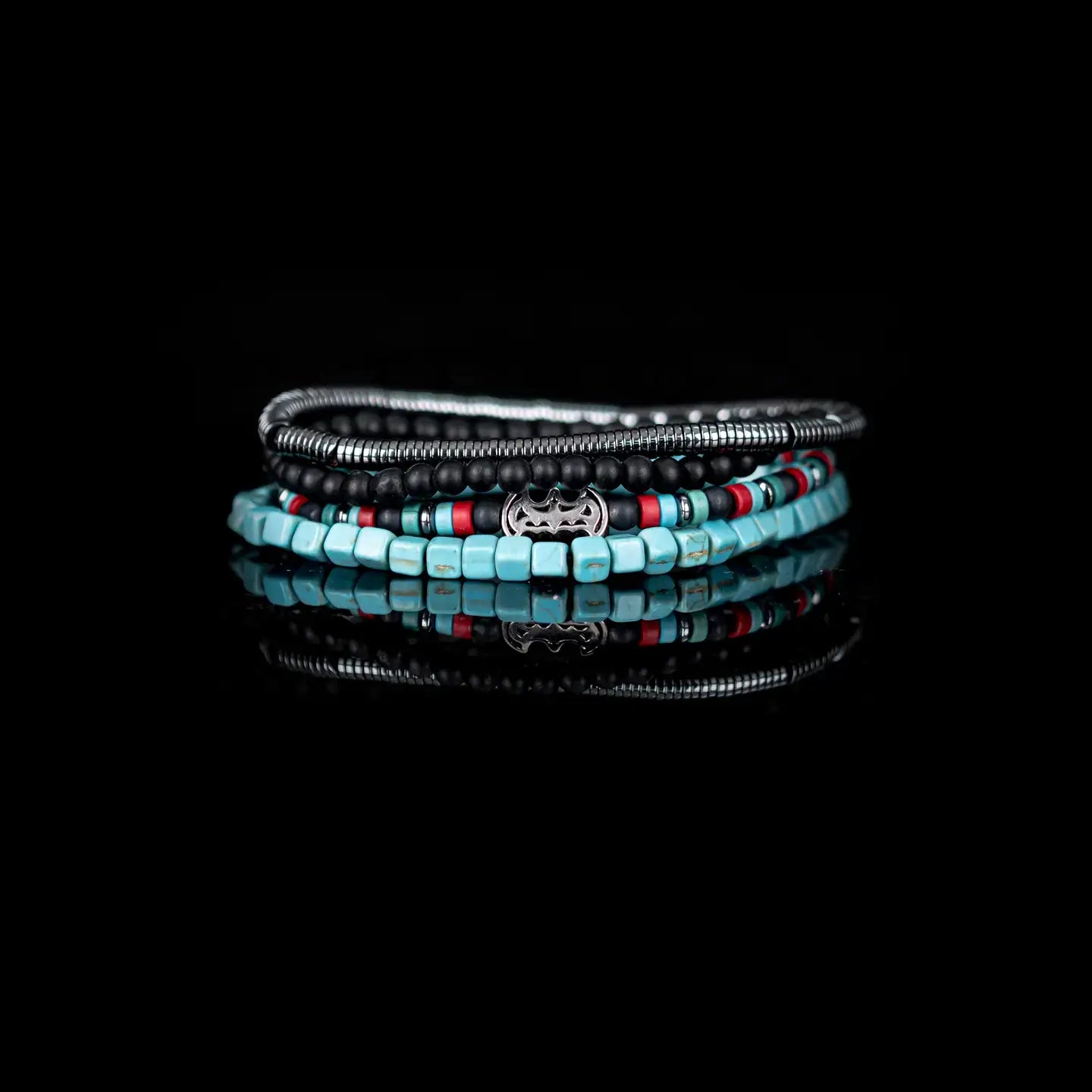 Black multi-layer men’s bracelet featuring matte black beads, turquoise cube beads, metallic hematite strands, red accent details, and crystal centerpiece accent on a light background.